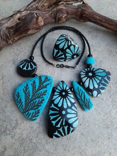 four pieces of blue and black jewelry on a stone surface next to a piece of driftwood