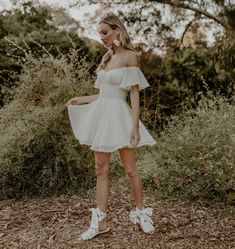 a woman standing in the woods wearing a white dress with ruffles on it