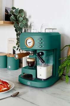 a green coffee maker sitting on top of a counter next to a plate of food