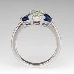 This timeless treasure is centered with an emerald cut diamond weighing 1.55 carats that is set into four-prongs. The shoulders of the ring are each accented with one (1) prong set, trillion cut natural sapphire. The ring measures 7.6mm at the top, rises 5.6mm above the finger, tapering to 2.9mm wide and 1.8mm thick at the base of the shank. It is currently a size 6. Timeless Sapphire Diamond Ring With Emerald Cut, Luxury Gia Certified Trillion Cut Emerald Ring, Luxury Gia-certified Trillion Cut Emerald Ring, Luxury Sapphire Ring With Three Stone Baguette Cut, Luxury Three-stone Sapphire Ring With Baguette Cut, Luxury Three Stone Sapphire Ring With Baguette Cut, Classic Trillion Cut Diamond Ring Gia Certified, Emerald Cut Sapphire Diamond Ring With Center Stone, Timeless Sapphire Baguette Cut Ring With Prong Setting