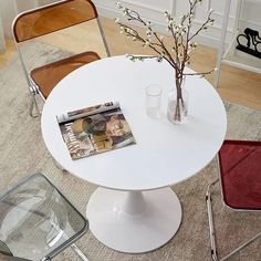 a white table with two chairs and a magazine on top of it next to a vase filled with flowers