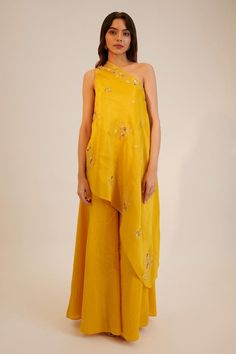 Yellow one shoulder asymmetric embroidered top. Paired with a silk kalidar pant. Components: 2 Pattern: Embroidered Type Of Work: Sequin, Thread Neckline: One-Shoulder Sleeve Type: Asymmetric Fabric: Tissue Georgette, Silk, Crepe Color: Yellow Other Details:  Attached lining Approx. product weight: 1kg Pant closure: Button Occasion: Mehendi and Haldi - Aza Fashions One Shoulder Suits Indian, One Shoulder Kurti, Pant Suits For Women Indian, One Shoulder Ethnic Dress, One-shoulder Embroidered Festive Sets, One Shoulder Haldi Outfit, Yellow Semi-stitched Unstitched Suit In Traditional Drape, One Shoulder Embroidered Festive Sets, Festive Summer Sets With Asymmetrical Hem