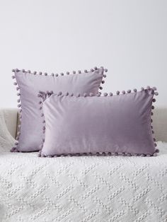 three pillows sitting on top of a bed next to a white pillow case with pom - poms