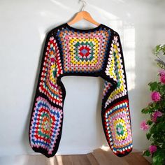 a colorful crocheted sweater hanging on a wall