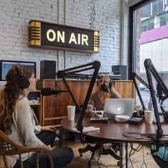 two women sitting at a table with laptops and headphones on in an office