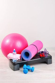 an exercise mat, water bottle and gym equipment on a wooden floor in front of a white wall