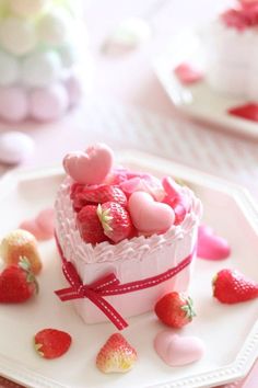 a white plate topped with a small cake covered in strawberries and candy heart shaped candies