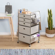 a metal cart with five drawers on wheels in front of a blue wall and potted plant