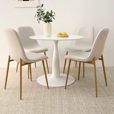 a white table with four chairs and a vase filled with lemons on the top