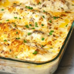 a casserole dish sitting on top of a table with green onions and cheese