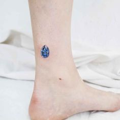 a woman's foot with a small blue tear shaped tattoo on her left ankle