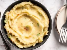 mashed potatoes in a black bowl with two forks next to it on a marble surface