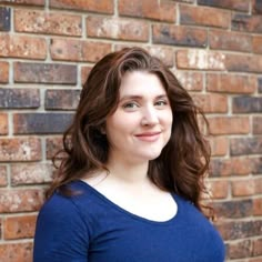 a woman standing in front of a brick wall with her hands on her hips and looking at the camera