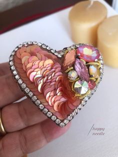 a person holding a heart shaped brooch in their hand