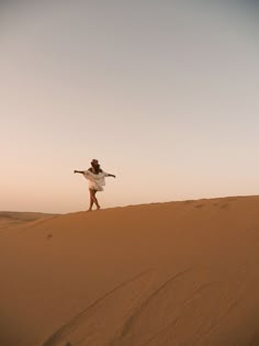 a woman standing on top of a sand dune in the desert with her arms outstretched