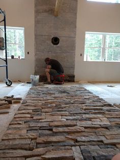 a man working on a brick wall in a room under construction with windows and ladders