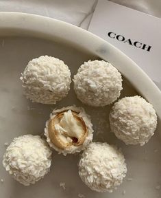 four coconut balls on a white plate with the word coach written in black across it