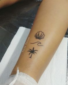 a woman's arm with a tattoo that has a palm tree and seashell on it