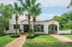 a white house with palm trees in the front yard and brick walkway leading up to it