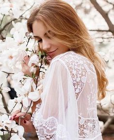 a beautiful young woman standing next to a tree with white flowers in her hair and wearing a lace top