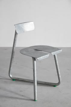 a metal chair sitting on top of a cement floor next to a white wall and green feet