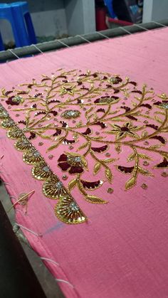 pink table cloth with gold embroidered design on the top and bottom, sitting on a machine