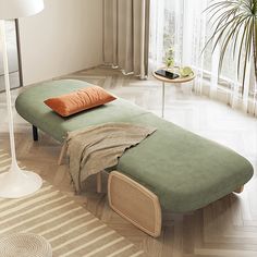 a green chaise lounge with an orange pillow on it in front of a large window