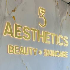 the sign for aesthetics beauty and skincare is lit up in gold letters on a white marble wall