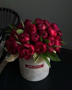 a white vase filled with red flowers sitting on top of a table next to a black chair