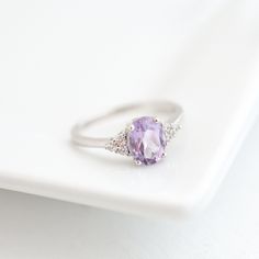 a white plate holding a ring with a purple stone in the middle and two diamonds around it