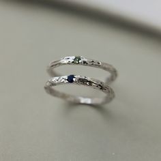 two silver rings sitting on top of a table next to each other with blue stones in them