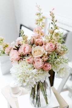 a vase filled with pink and white flowers on top of a table next to a mirror