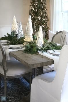 a dining room table decorated for christmas with white trees and greenery on the top