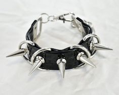 "This product is a handmade cuff, created from faux leather/vegan leather. All metal accessories are made of stainless steel (spikes, rivets, D-rings, chain, lobster claw). All charms and pendants are made of glass. Sizes are adjustable: Small: 6-7.5 inches Medium: 7.5-9 inches If you wish to purchase a pair of cuffs, choose the \"x2\" option with the correct size for a discount!" Edgy Leather Choker Jewelry, Edgy Leather Choker, Punk Leather Jewelry With Rivets, Punk Jewelry With Spikes, Punk Jewelry With Spikes For Alternative Fashion, Edgy Silver Leather Bracelet, Edgy Silver Leather Bracelet With Spikes, Punk Jewelry With Studs For Concerts, Punk Studs Jewelry For Concerts