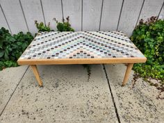 a wooden table sitting on top of a sidewalk next to green bushes and shrubbery