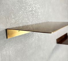 a gold shelf mounted to the side of a wall with two hooks on it and water droplets coming out of them