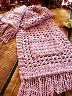 a pink knitted scarf sitting on top of a wooden table next to dried flowers