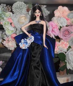 a barbie doll wearing a blue and black dress with flowers in the background on display