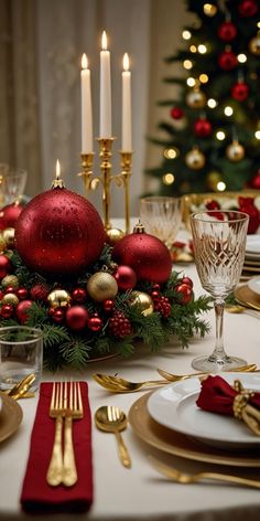 a christmas table setting with red and gold ornaments, silverware, candles and plates