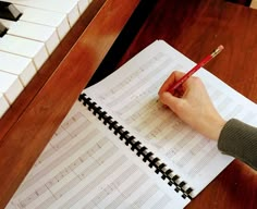 a person holding a pencil and writing on a sheet of paper with piano keys in the background