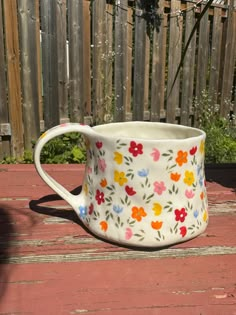 a flowered mug sitting on top of a wooden table next to a garden fence