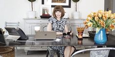 a woman sitting at a table with a laptop computer in front of her and flowers behind her