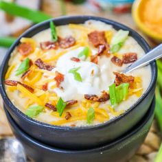 a close up of a bowl of soup with cheese and bacon on top, along with green onions