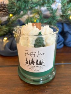 a glass jar filled with marshmallows and frosted pine trees on top of a wooden table