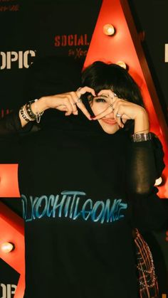 a woman making a heart sign with her hands while standing in front of a red wall