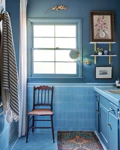 a blue tiled bathroom with a chair in the corner and a rug on the floor