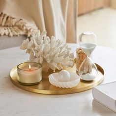 a tray with candles, seashells and an hourglass sitting on a table