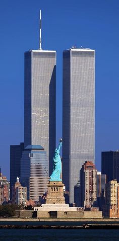 the statue of liberty stands in front of two tall skyscrapers that rise high into the sky