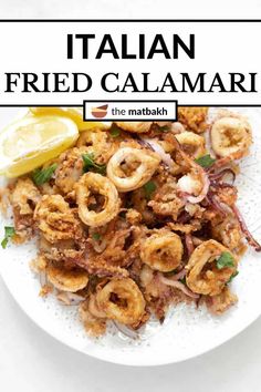 a white plate topped with fried calamari next to a lemon wedge