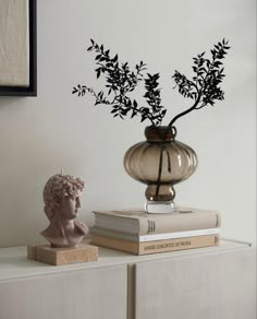 a vase filled with flowers sitting on top of a book shelf next to a busturine